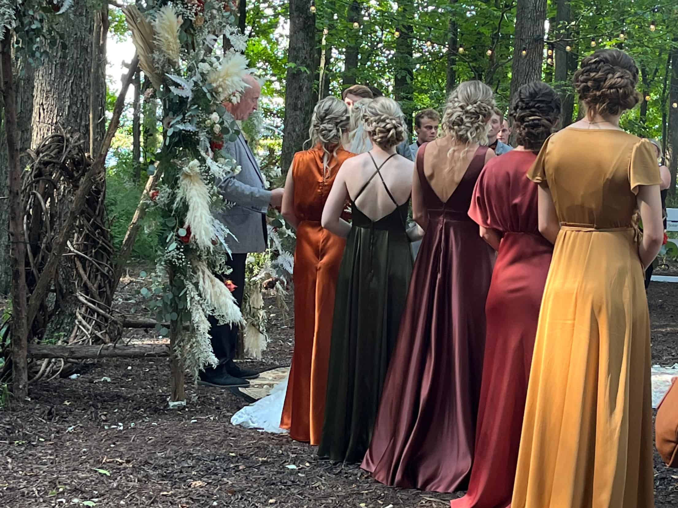 Bridal party in fall-toned dresses at a forest ceremony at Highland Oaks
