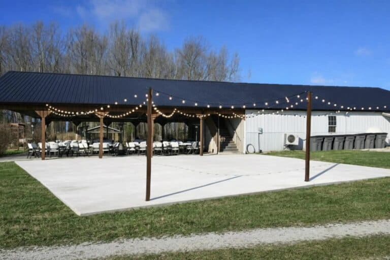 Tables and chairs set under the string lights of the covered pavilion at Highland Oaks in Palmyra, Indiana, ready for a wedding reception