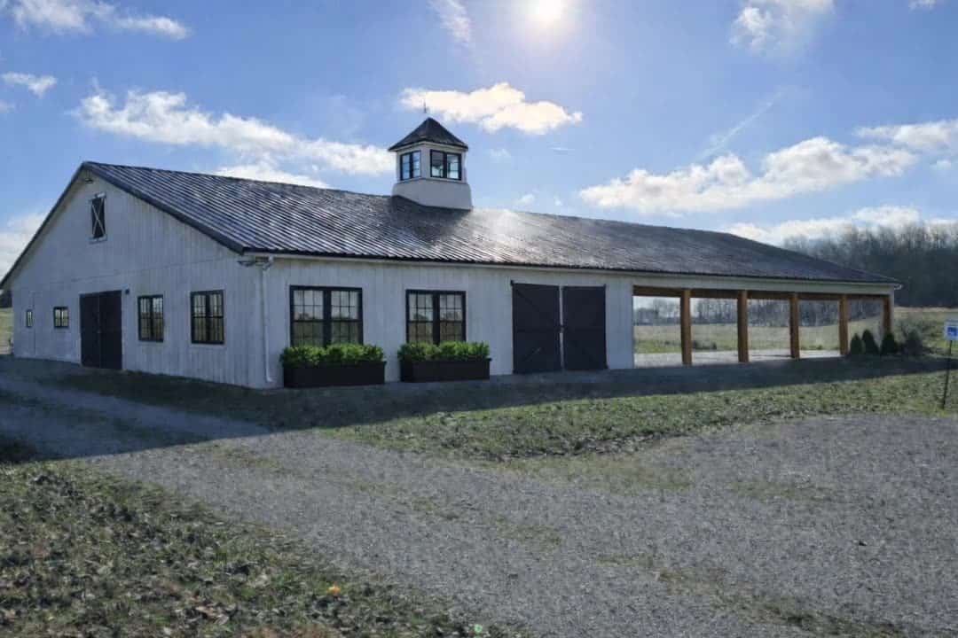 The white barn with cupola and attached covered pavilion under afternoon sun at Highland Oaks Weddings and Events in Palmyra, Indiana