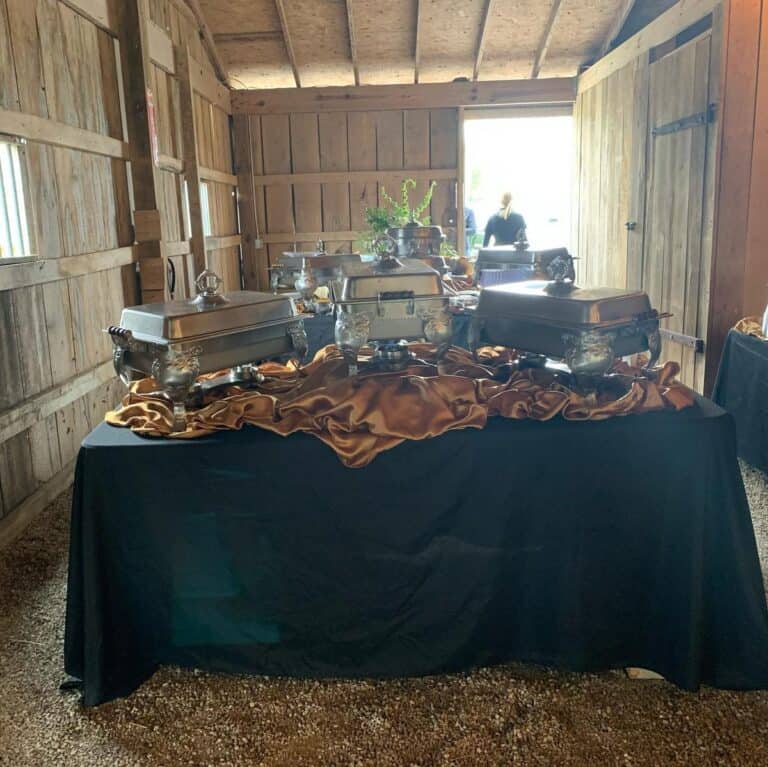 Caterer buffet line of silver chafing dishes on a black-draped table inside the barn at Highland Oaks in Palmyra, Indiana