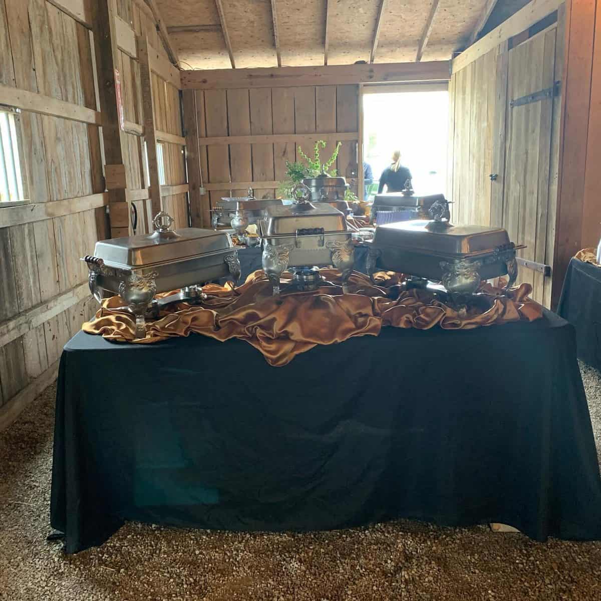 Caterer buffet line of silver chafing dishes on a black-draped table inside the barn at Highland Oaks in Palmyra, Indiana