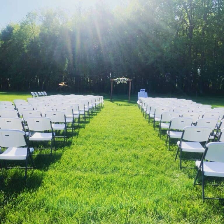 Rows of white folding chairs set on the lawn facing a wooden arbor at the tree line at Highland Oaks in Palmyra, Indiana, before guests arrive