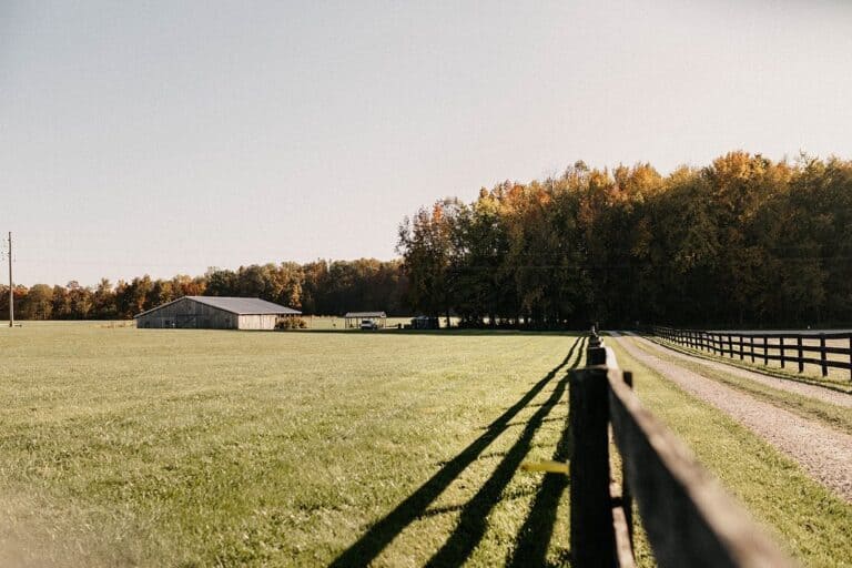 Long fence shadows across the field at Highland Oaks in Palmyra, Indiana, with the barn and oak treeline in late day light