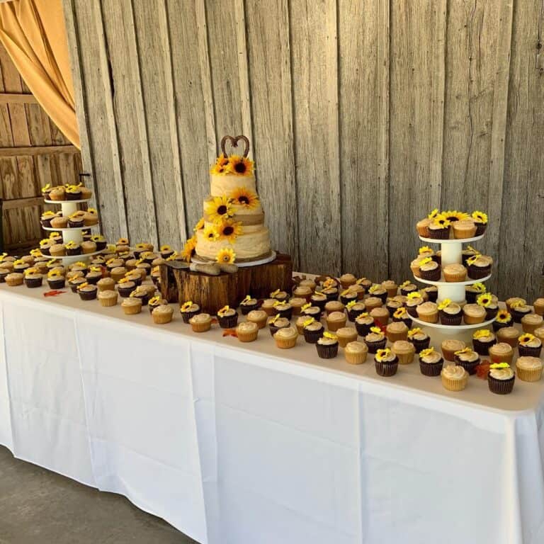 Dessert table in the Highland Oaks barn with a sunflower wedding cake and rows of cupcakes