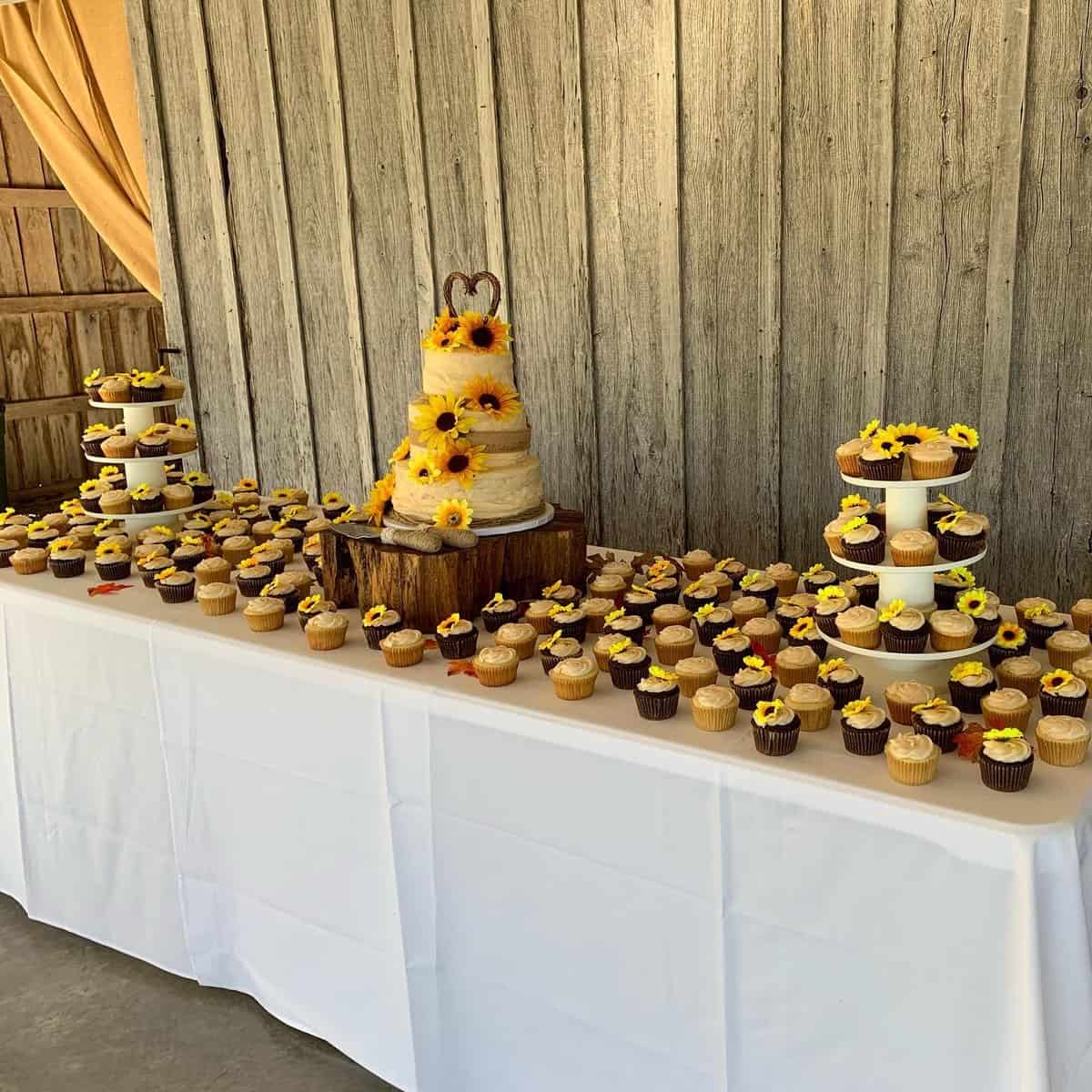 Dessert table in the Highland Oaks barn with a sunflower wedding cake and rows of cupcakes